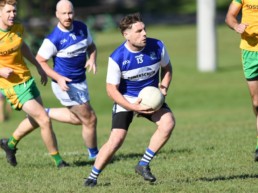 men's gaelic player runs with ball during game with teammate in background